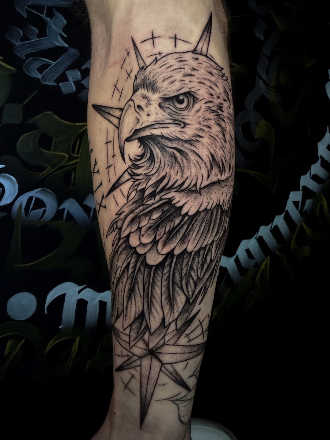 Zwart-grijze tattoo van een adelaarskop met kompasster op een onderarm.